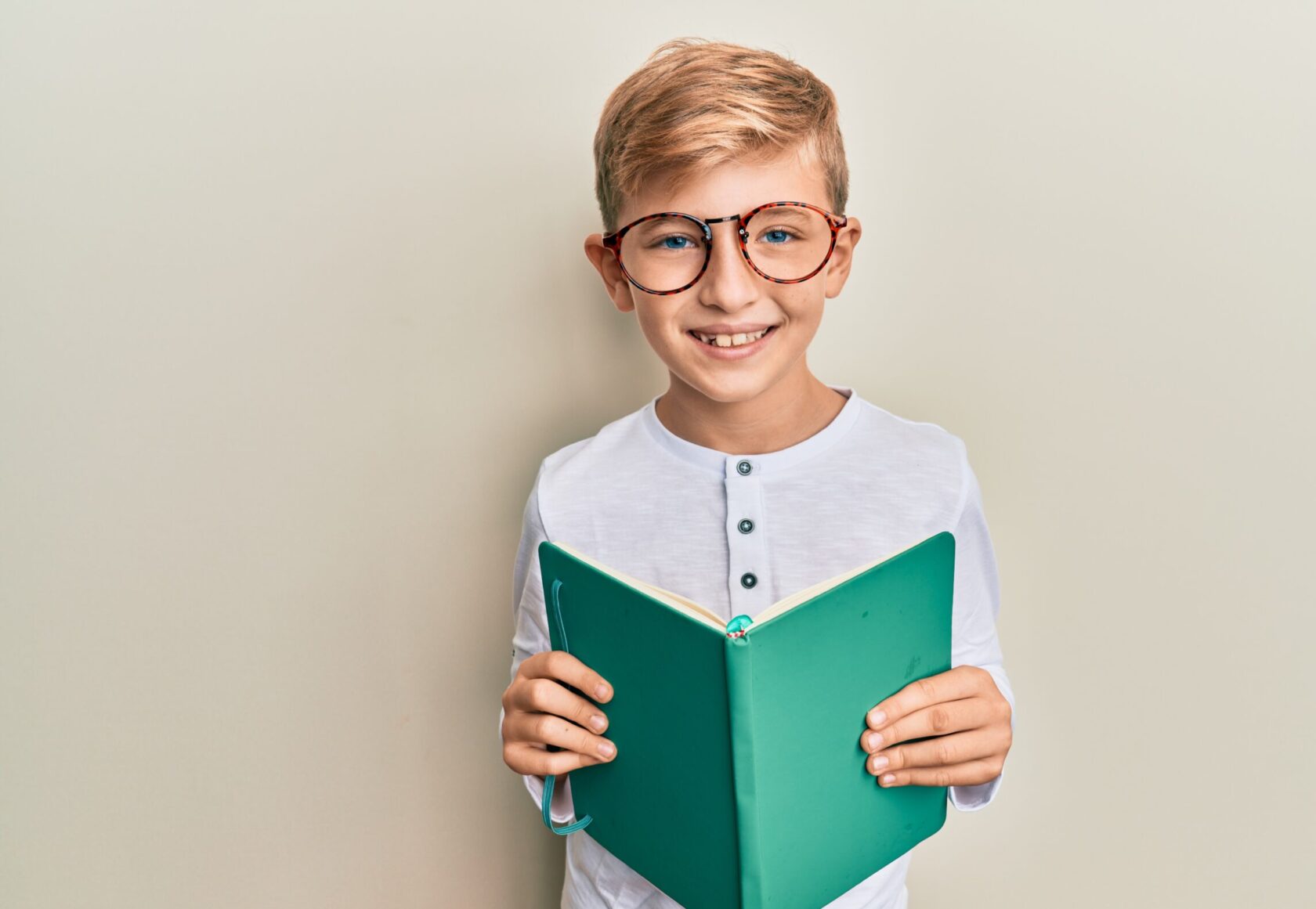 Little caucasian boy kid reading a book wearing glasses smiling with a happy and cool smile on face. showing teeth.